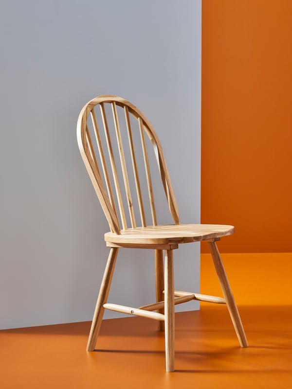 A SKOGSTA chair, in traditional style, is placed against a beige wall in a space with bright orange floors.