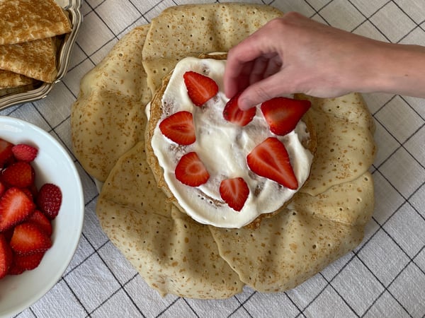 Närbild på en person som lägger skivade jordgubbar på en pannkakstårta.