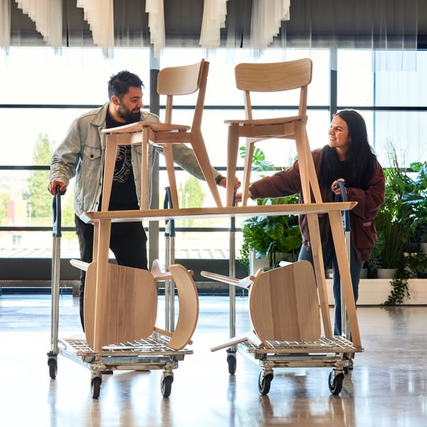 Two people transporting a table and chairs on a cart