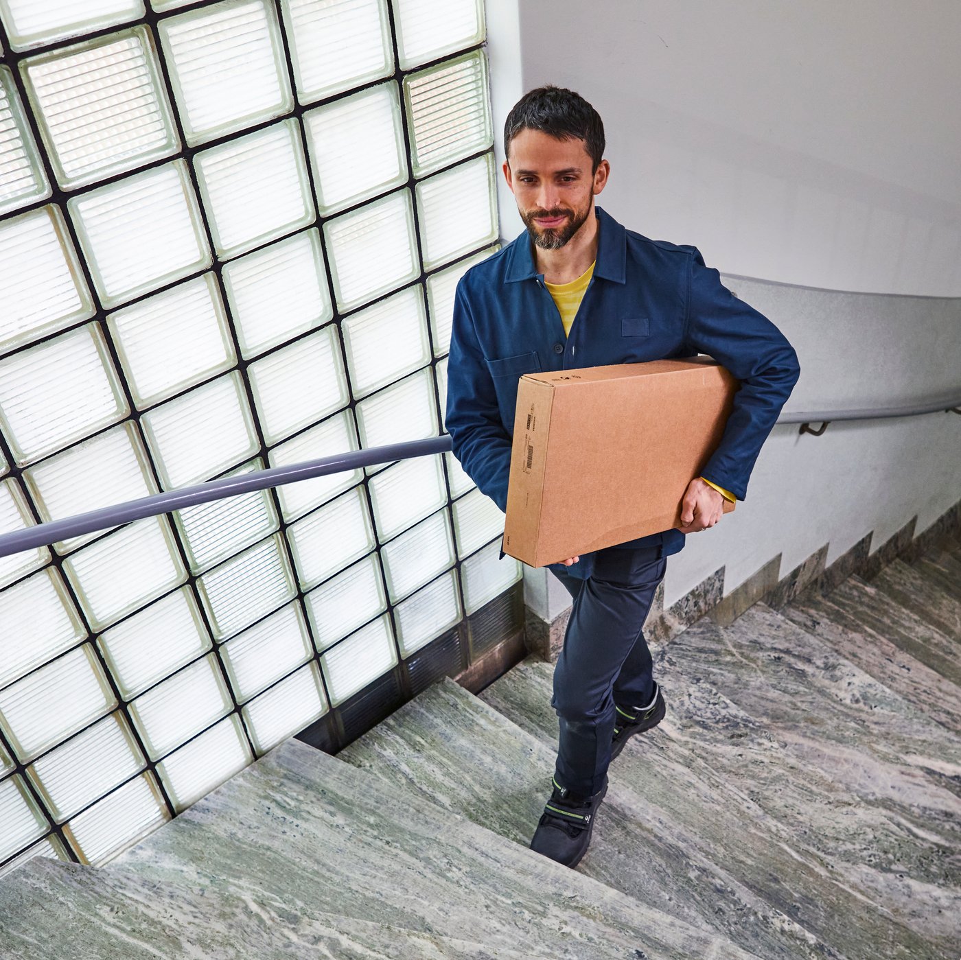 Ein Lieferant im Treppenhaus, der ein Päckchen nach oben trägt.