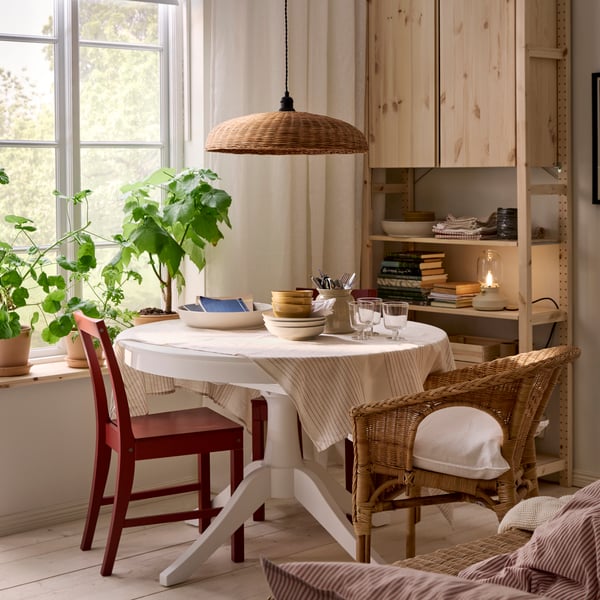 Table ROSENTORP blanche entourée de chaises différentes, près d’une fenêtre et devant une étagère IVAR. Des plantes sur le rebord d’une fenêtre.