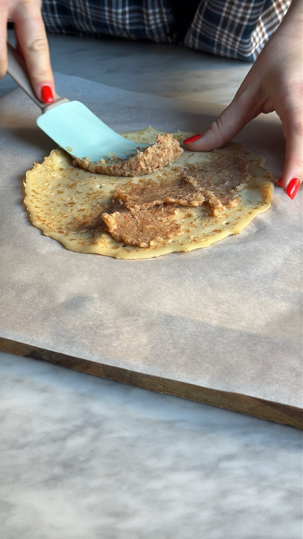 En person brer på mandelmassa på en pannkaka med hjälp av en BAKGLAD slickepott.