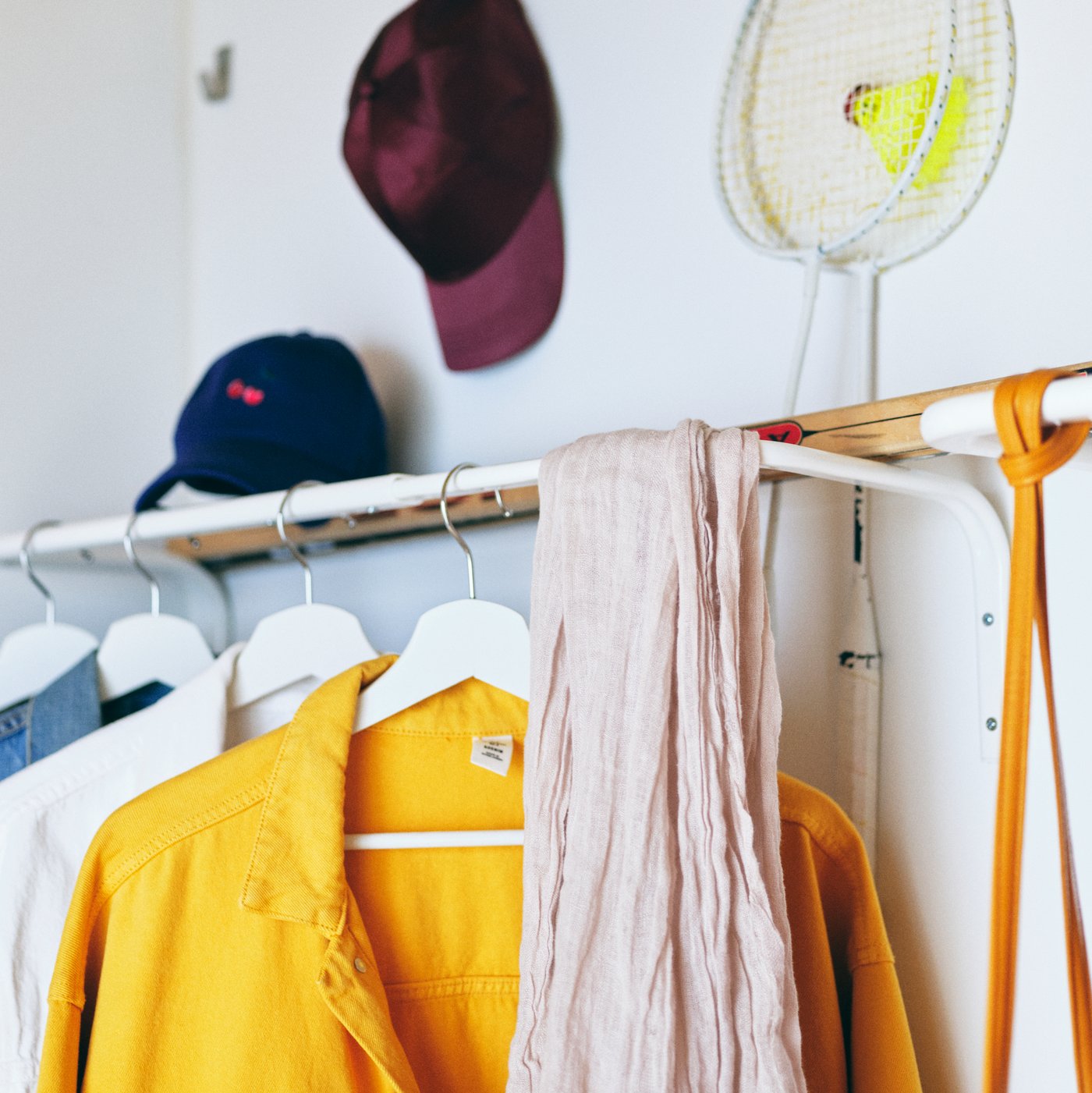 A hallway wall with clothes on white hangers, scarves, hats and accessories, all on and around a white MULIG clothes bar.