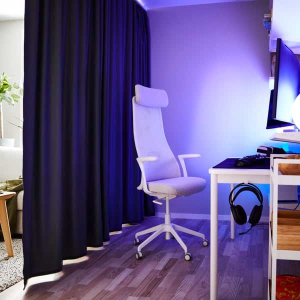 Mit Verdunklungsgardinen an Gardinenschienen lässt sich der Raum in Wohnzimmer und Gaming-Ecke mit einem Drehstuhl in Weiß/Beige aufteilen.