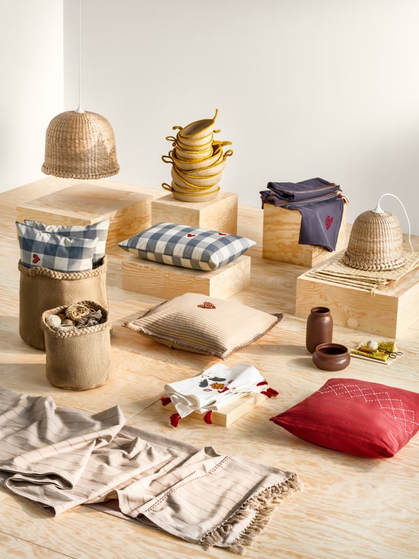 Some pieces from the MÄVINN collection are placed on a plywood surface: cushions, lampshades, baskets, curtains and more.