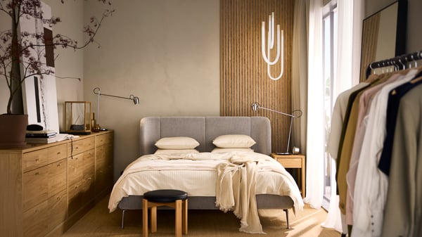 A bedroom with a dark green upholstered bed frame, 2 white pendant lamp shades, white bedding and a gray bedspread.