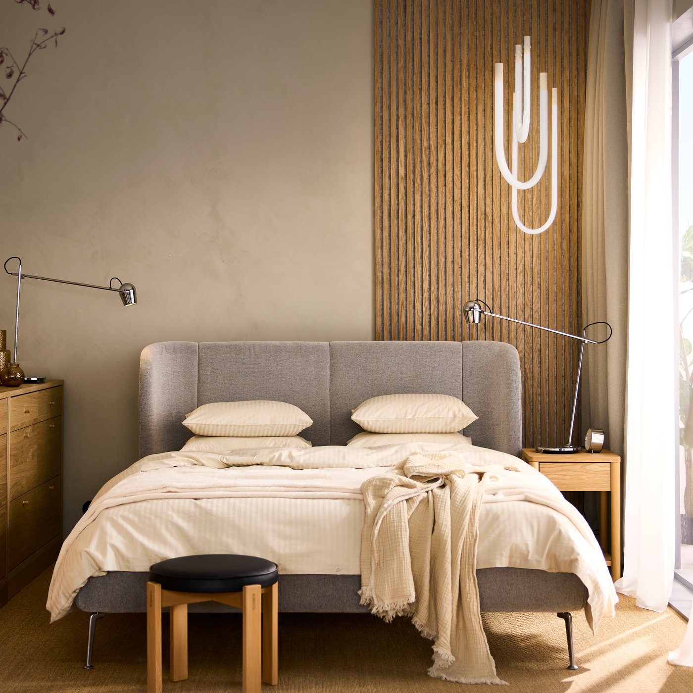 A TUFJORD double bed with storage with a VARMBLIXT LED pendant lamp hanging above it and a MODERMOLN work lamp by the side.