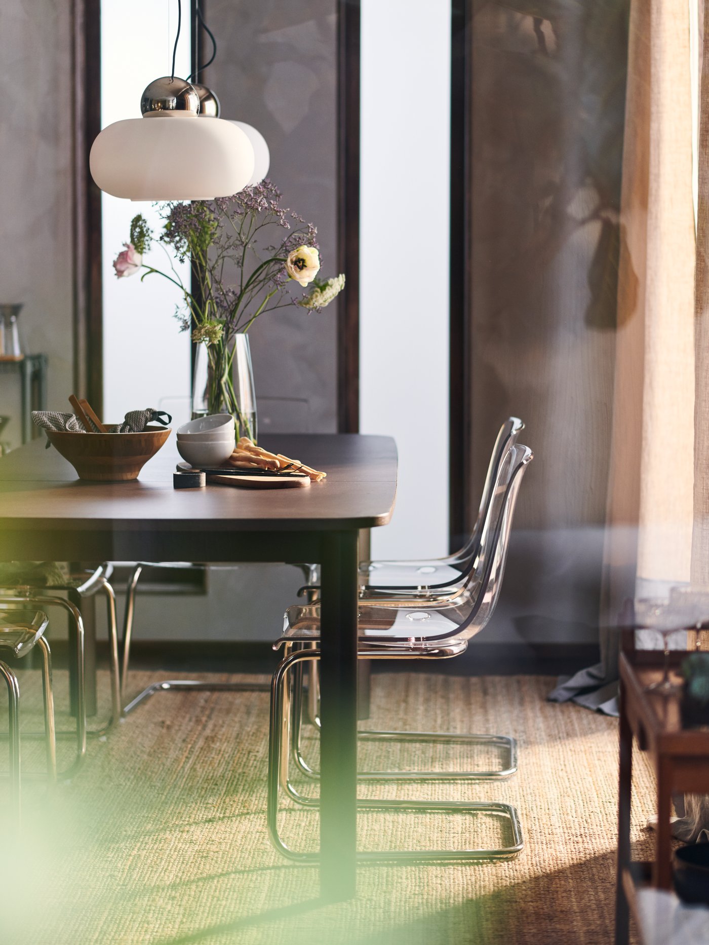 Una mesa extensible STRANDTORP en una habitación brillante con sillas TOBIAS a su alrededor y dos lámparas de techo DEJSA blancas encima.