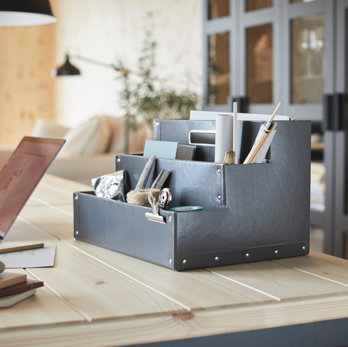 A grey desk organiser holding pencils, small notebooks and other diverse items.