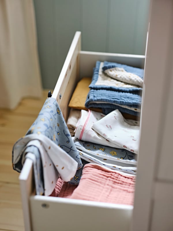 An open drawer holds a mix of folded bed linen including a blue/white dotted GULDVÄVARE blanket and GULDVÄVARE bed linen.
