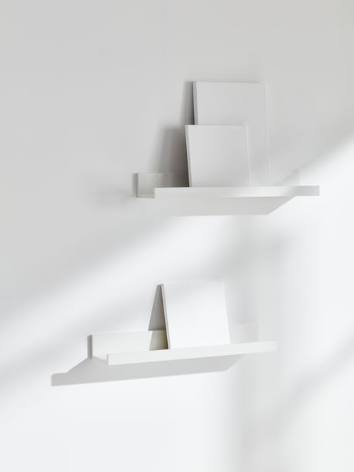 Two white MOSSLANDA picture ledges are mounted on a white wall and casting shadows. They hold blank, white canvasses.