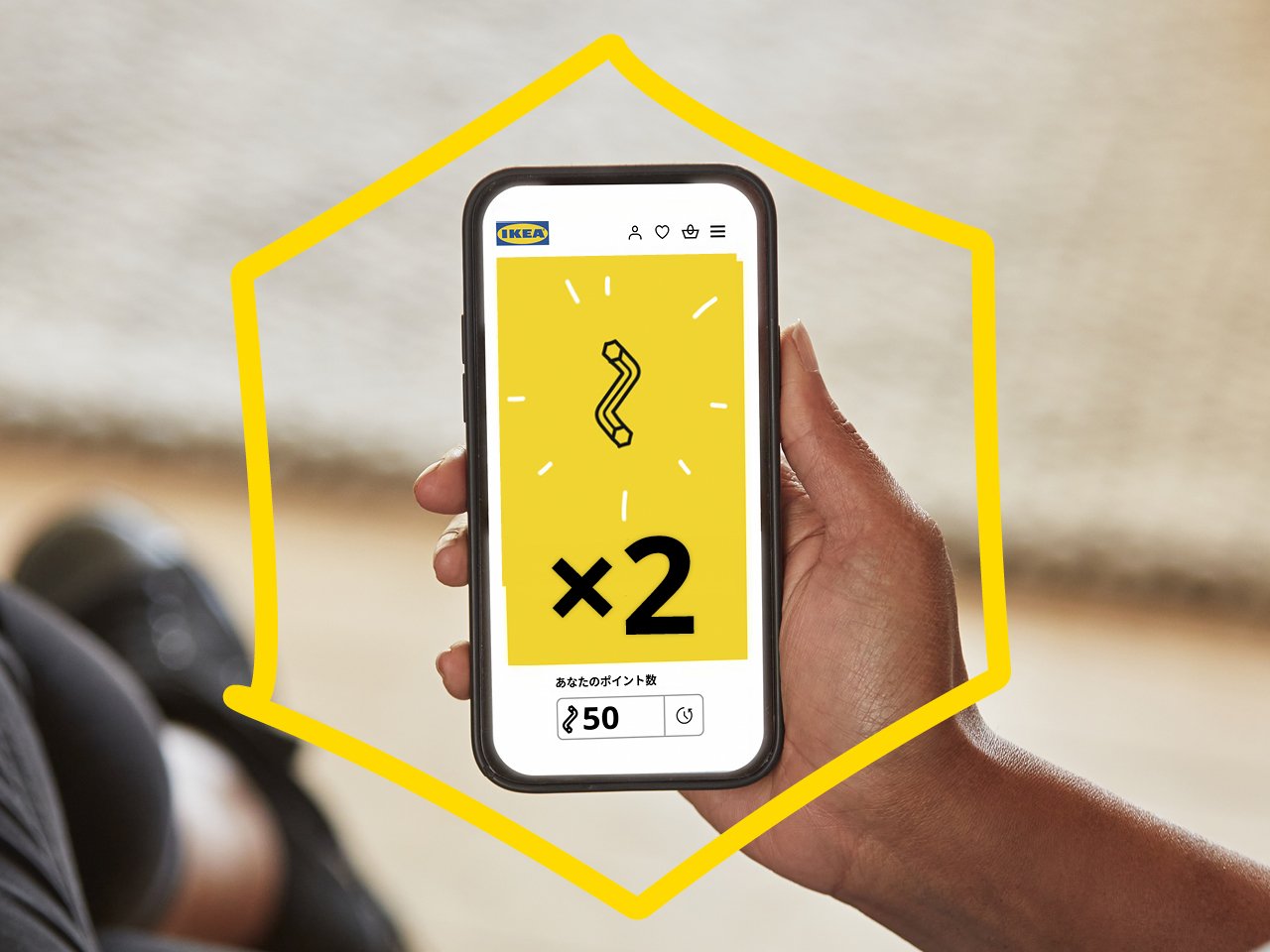 A hand holds a smartphone showing a yellow IKEA screen with a double points icon and 50 points displayed.