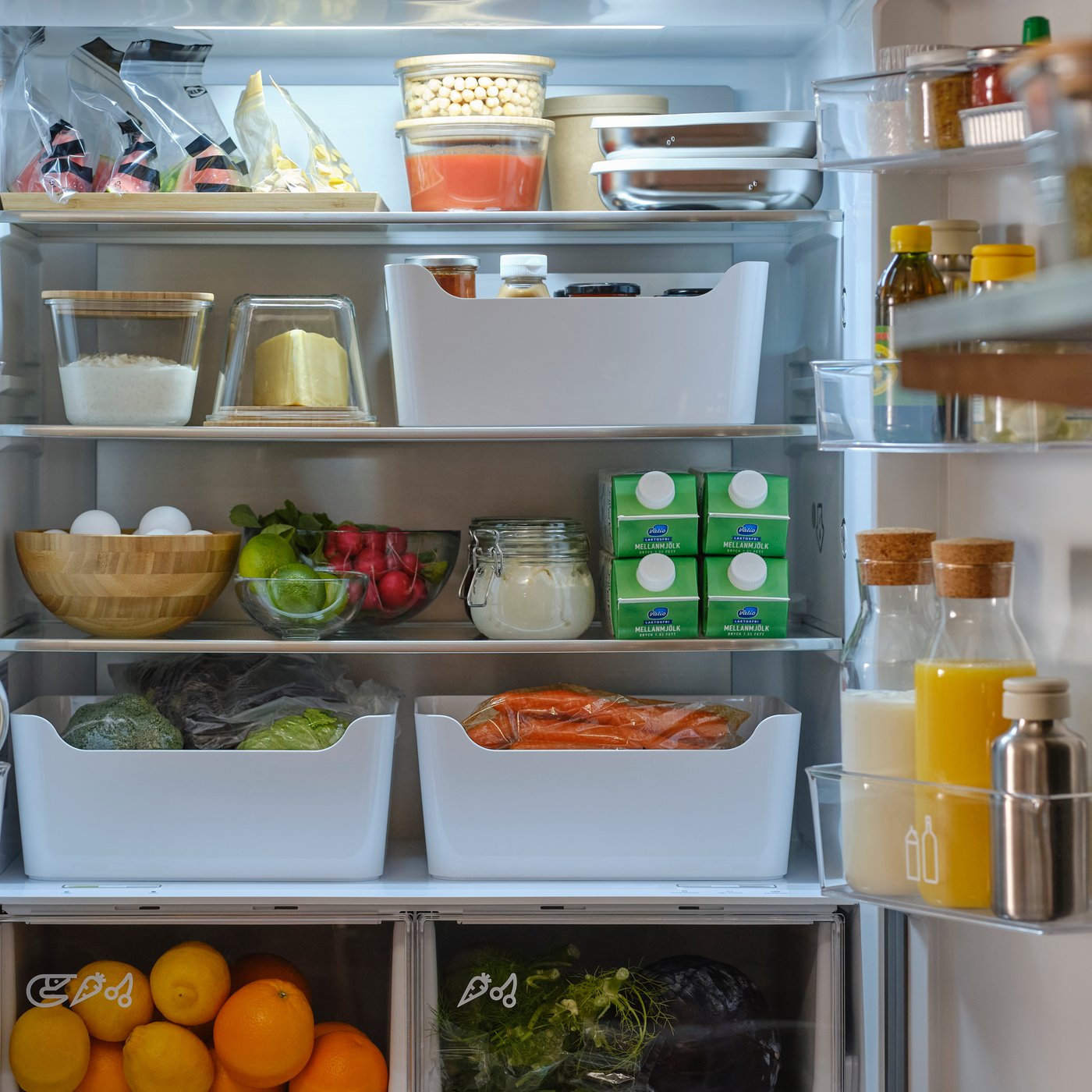 A fridge door is open and there are storage boxes, interior organisers and food items in glass containers and plastic bags.