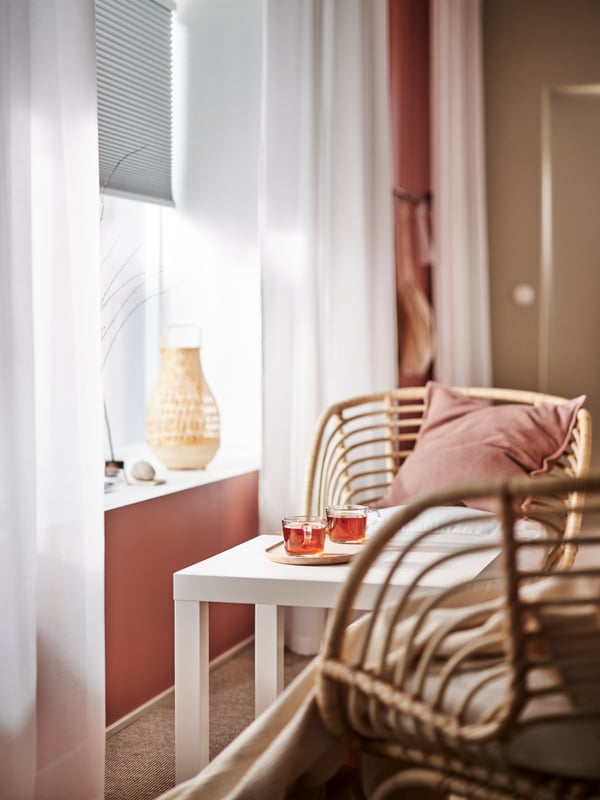 A white LACK side table, with a serving tray with two IKEA 365+ mugs on it, stands near a window with a blind halfway down.