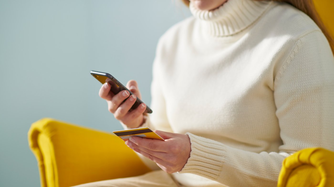 A person with a credit card paying sitting on a yellow STRANDMON armchair.