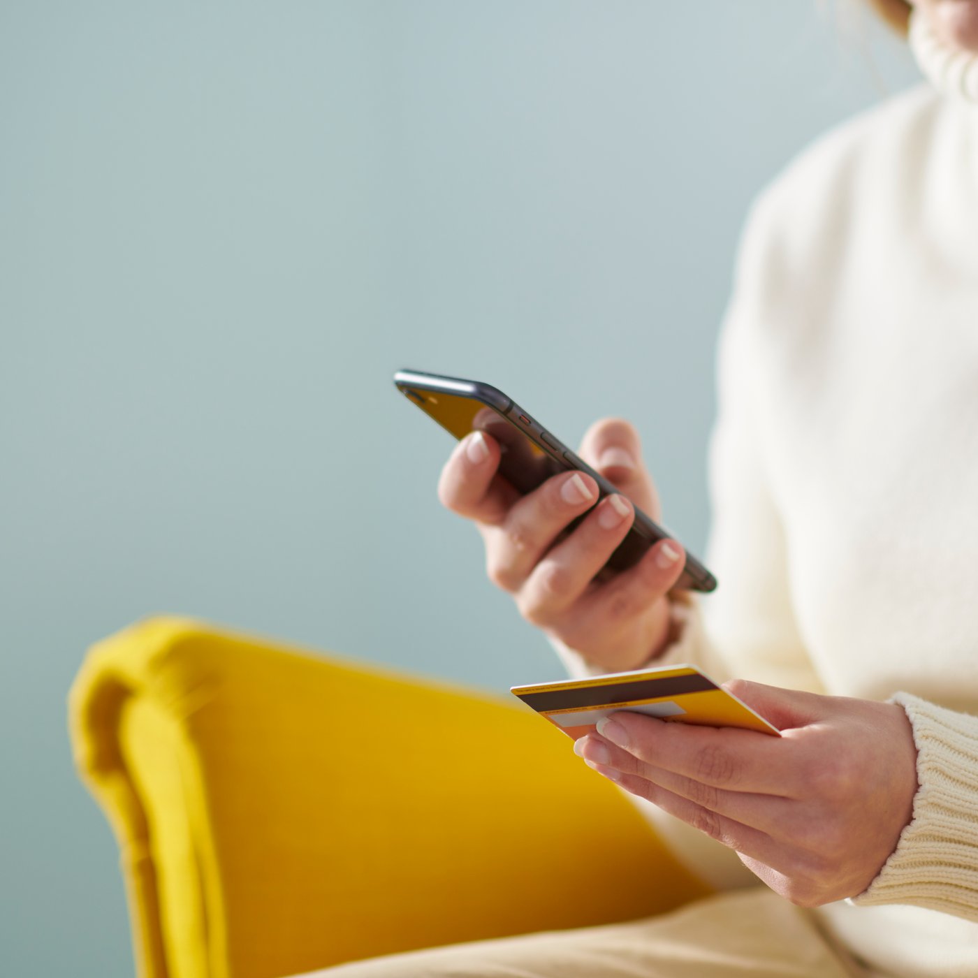 Person is sitting on yellow armchair with credit card and phone in hands.