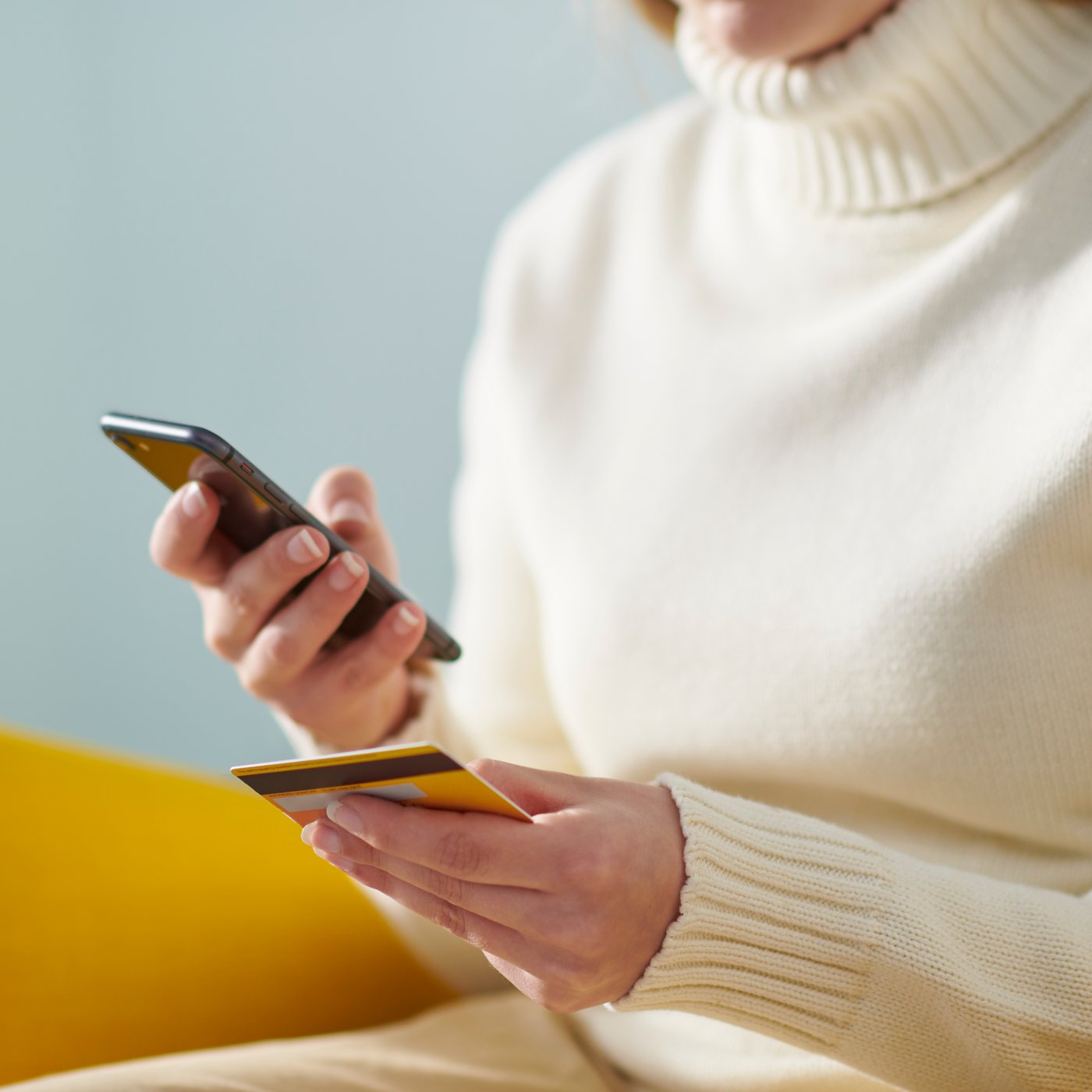 En dame som holder en betalingsløsning og sitter på en gul STRANDMON ørelappstol.