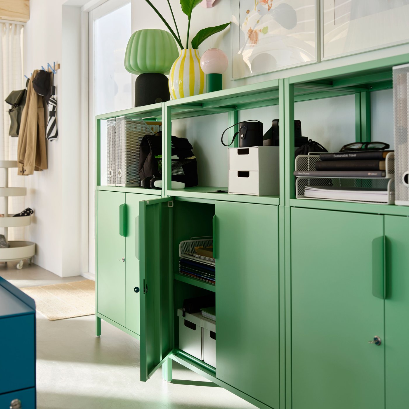 Row of green office cabinets with open shelving above. One cabinet door is open, revealing stationery stored inside.