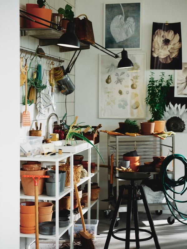 A planting area with a black DALFRED bar stool in front of a white/Glypen tap ENHET/TVÄLLEN open wash-stand with 2 shelves.