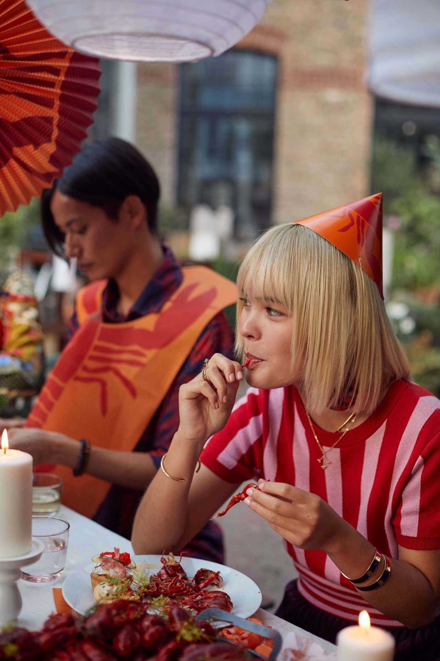 Groupe d’amis assemblés autour d’une table décorée pour la fête des écrevisses, sous des guirlandes de papier accrochées aux branches d’un arbre.