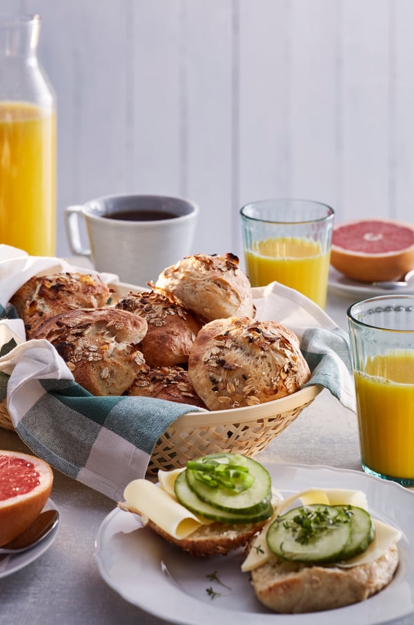A basket of rolls made with MÜSLI muesli on a breakfast table by a cup of coffee, orange juice and half a grapefruit.