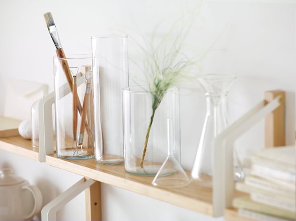 Several transparent glass CYLINDER vases on a wooden shelf against a white wall in the living room.