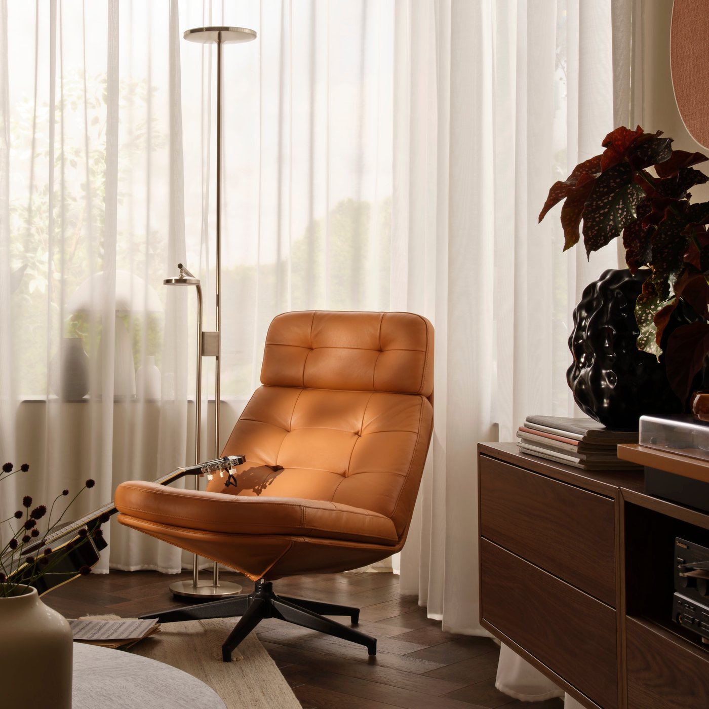 A living-room corner with a golden-brown HAVBERG swivel armchair beside a large window with STENFRÖ sheer curtains.