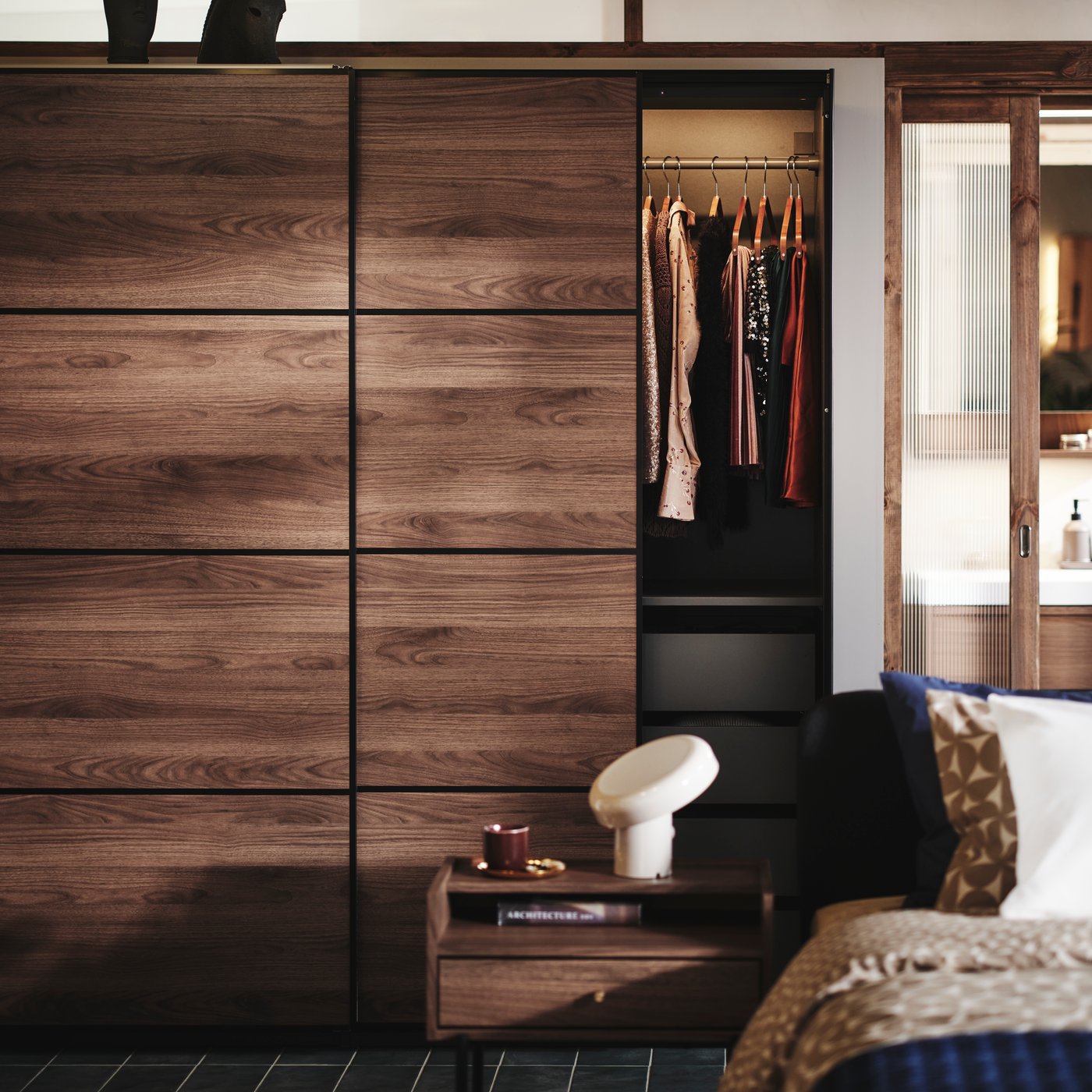 Ett sovrum med en RÅDMANSÖ byrå och ett sängbord samt en PAX MEHAMN garderob i bakgrunden. Alla möbler i mörkt trä.
