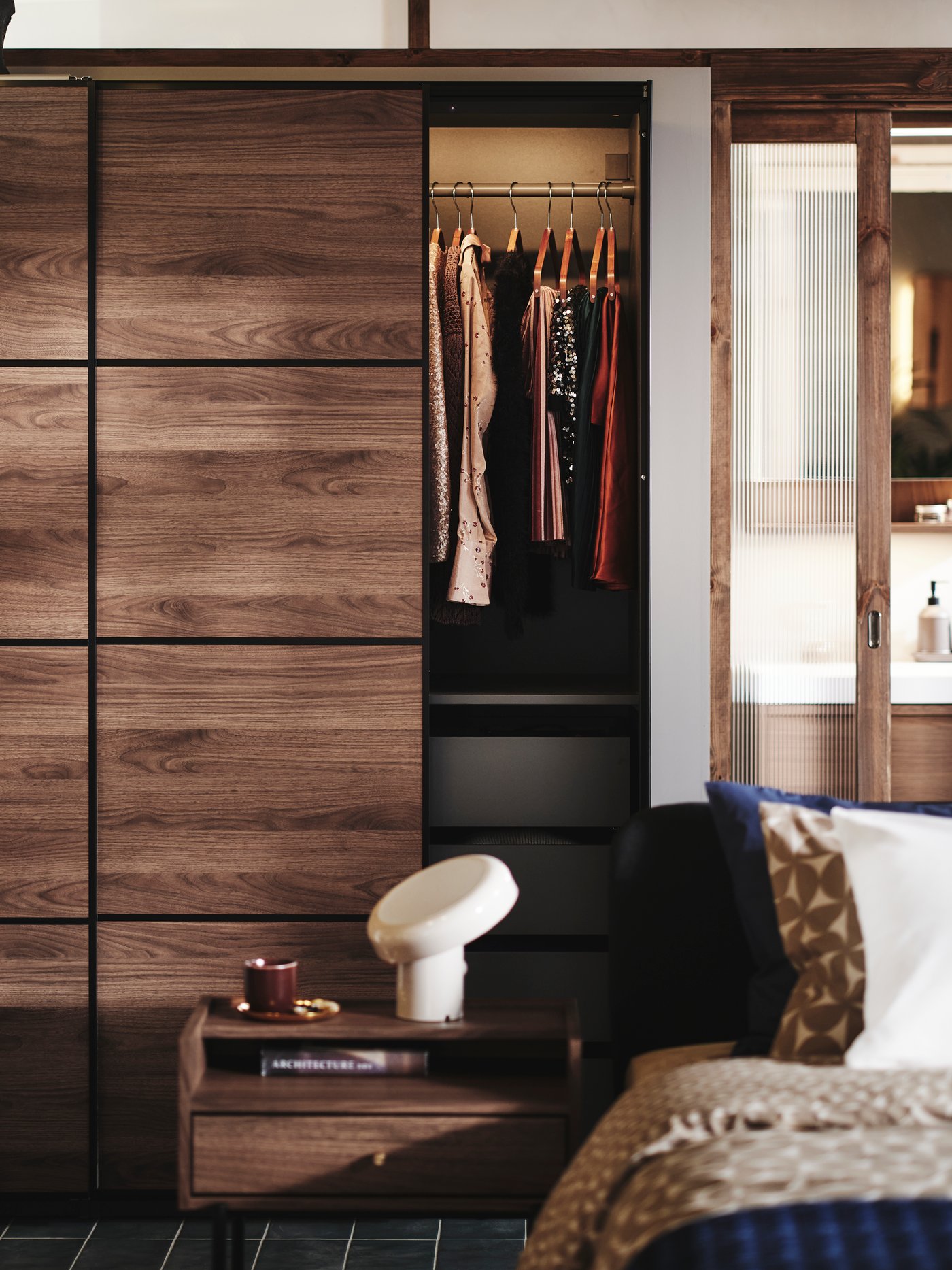 A bedroom with RÅDMANSÖ chest of drawers and bedside table plus PAX MEHAMN wardrobe in the background. All in dark wood.