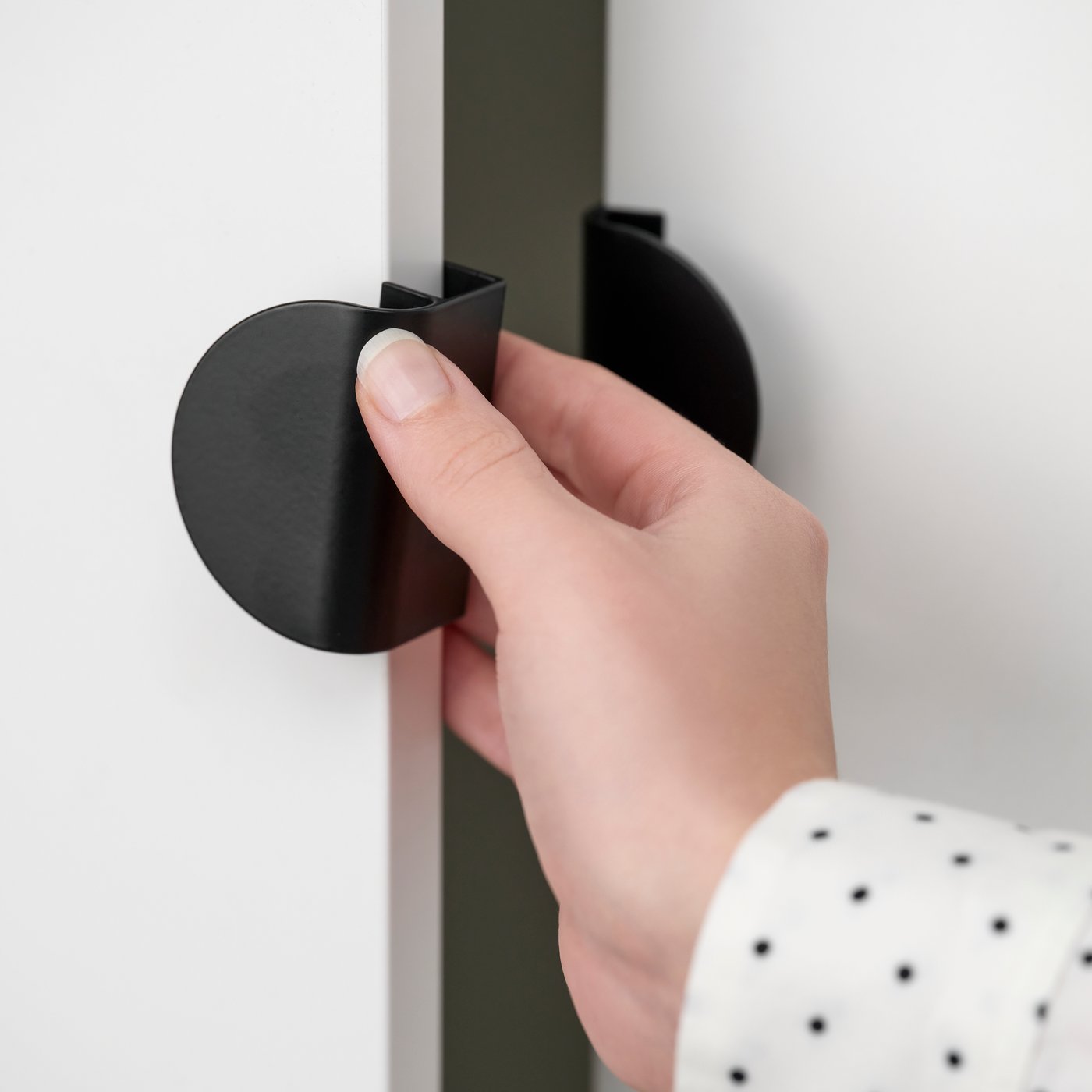 Hand opening a white cabinet door with a black circular pull handle.