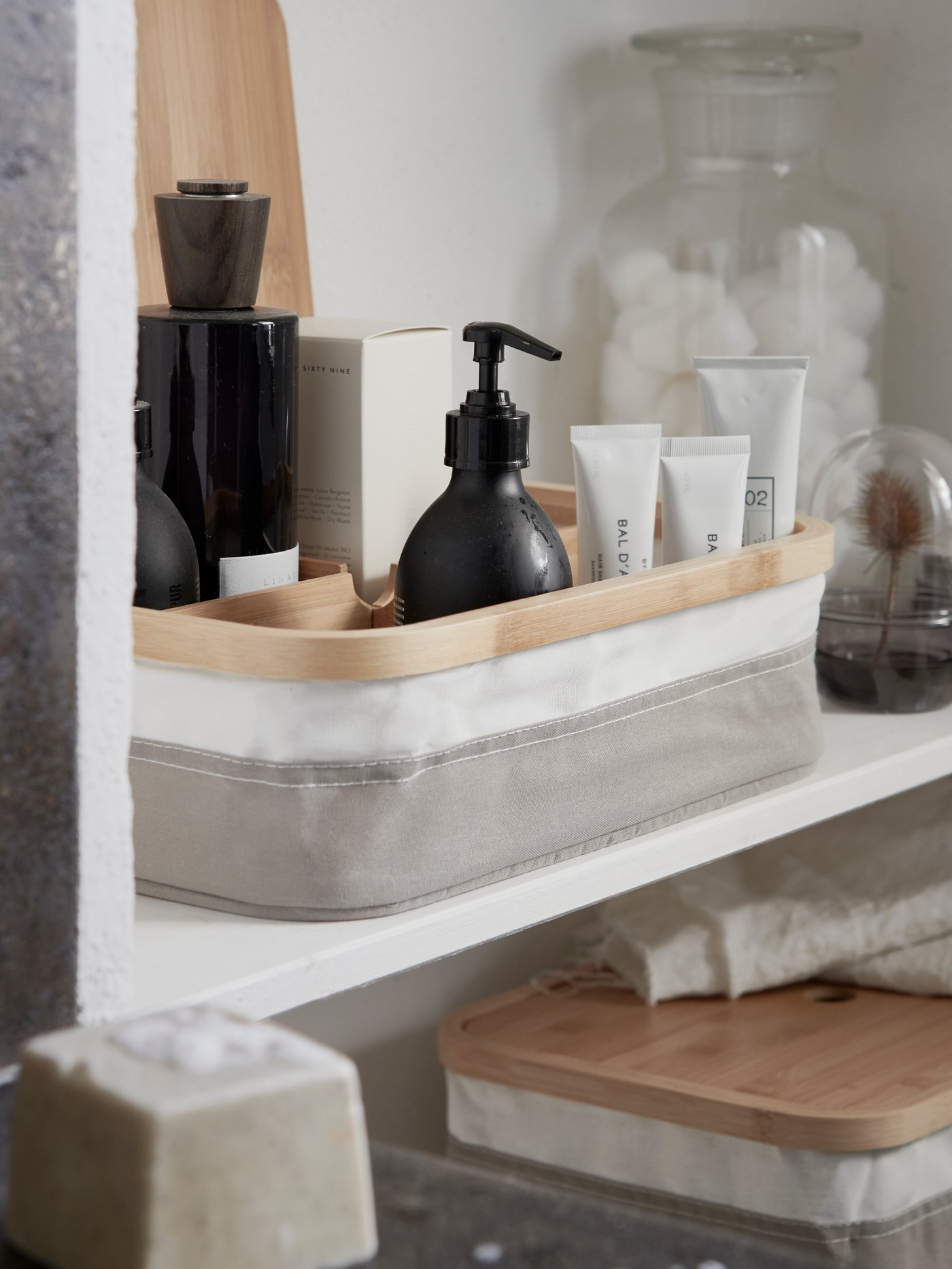 Beauty products ordered in a box with compartments, sitting on a wall shelf together with other elegant storage.