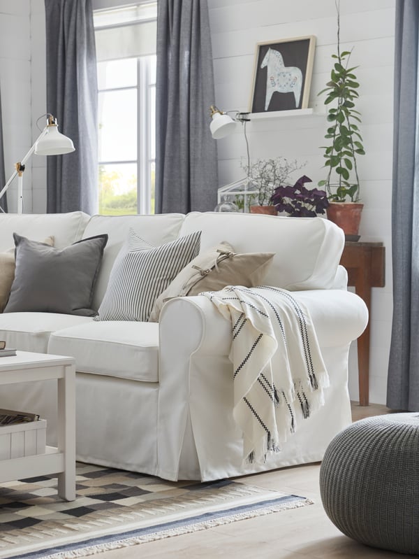 Un jeté STINAMAJ en coton, blanc et gris foncé, est posé sur le bras d’un canapé UPPLAND blanc dans un salon.