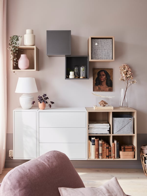 A wall with a combination of EKET cabinets with ceramics, glassware, books and other personal items placed in and on them in the living room against a beige wall.