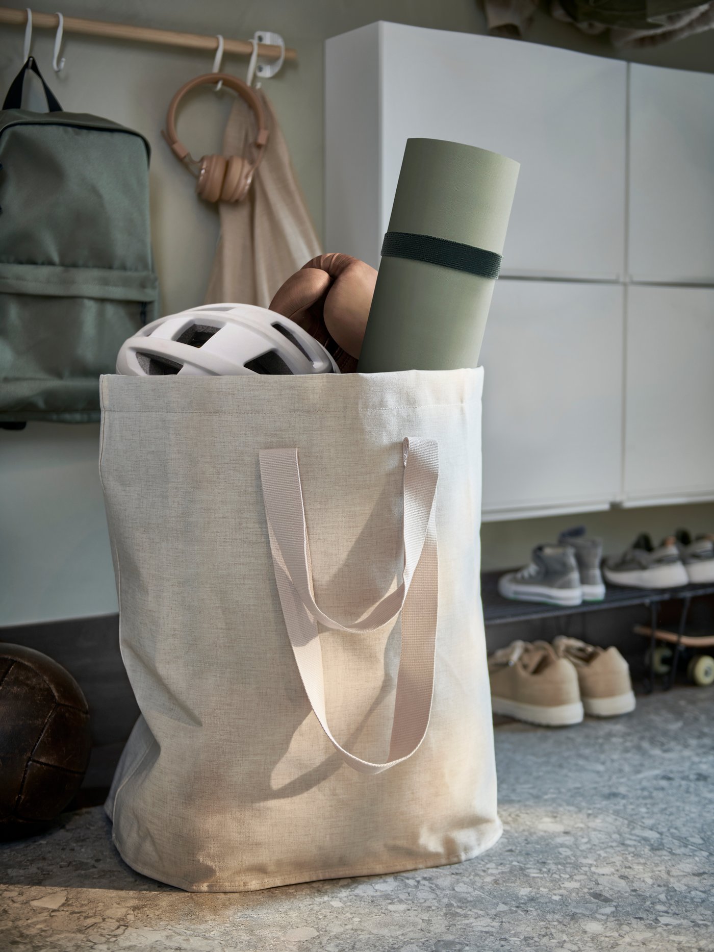 Primer plano de una bolsa para ropa PURRPINGLA junto a un zapatero con un estante para zapatos debajo y una barra con ganchos.