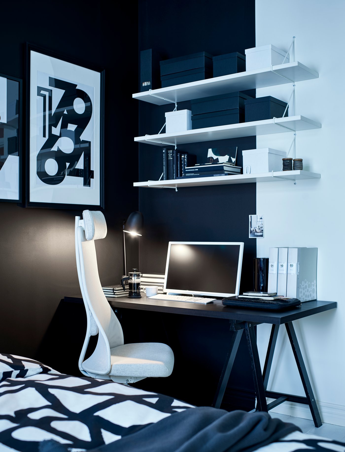 Silla blanca JÄRVFJÄLLET detrás de un escritorio negro LINNMON, encima de este un organizador blanco TJENA. En el fondo, una muralla pintada blanco/negro con una repisa BERGSHULT y al lado un cuadro RIBBA. 