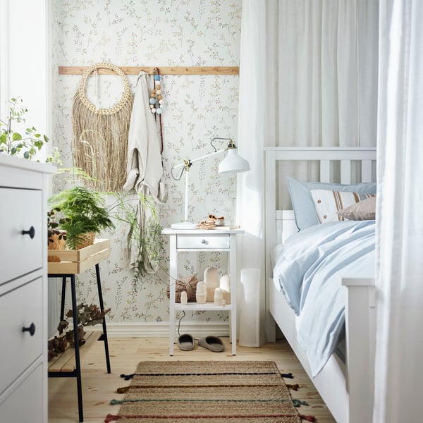 A HEMNES bed stands against a wall in a bedroom next to a HEMNES bedside table and opposite a HEMNES chest of 3 drawers.