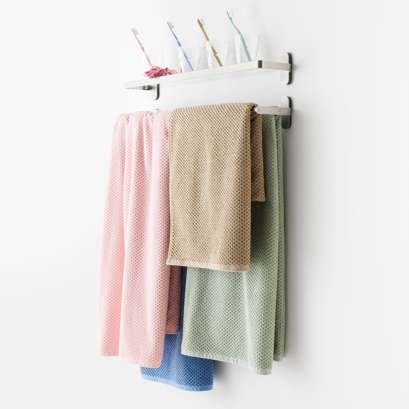 Négy, különböző színű GULVIAL törülköző egy tartón. A törölközők színei: rózsaszín, bézs, zöld és kék. A felettük lévő polcon ugyanilyen színű fogkefék találhatók.