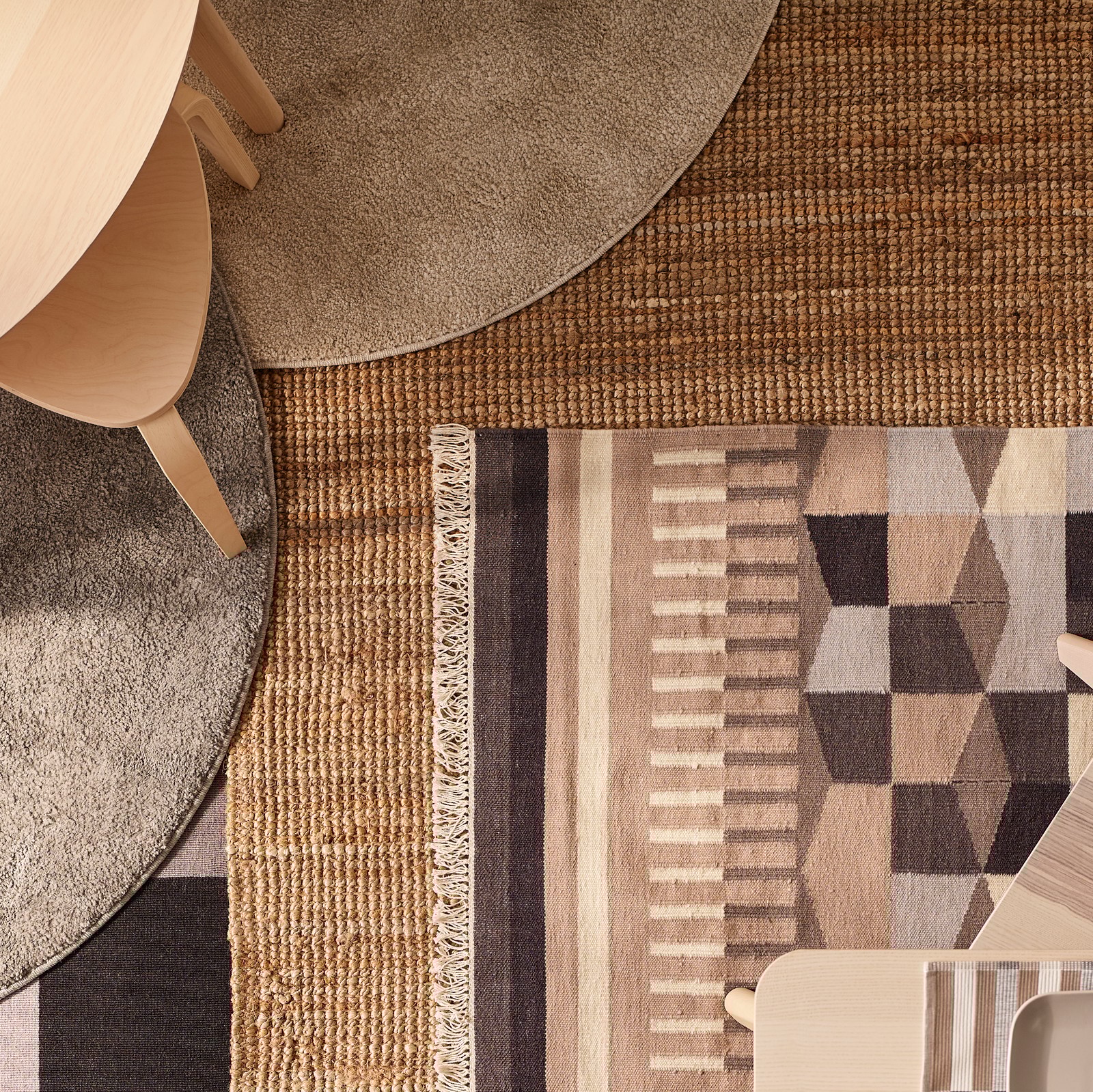 Două mese și scaune LISABO din furnir de frasin aflate pe o podea cu diverse covoare, inclusiv cu un covor LOHALS și câteva covoare cu model.