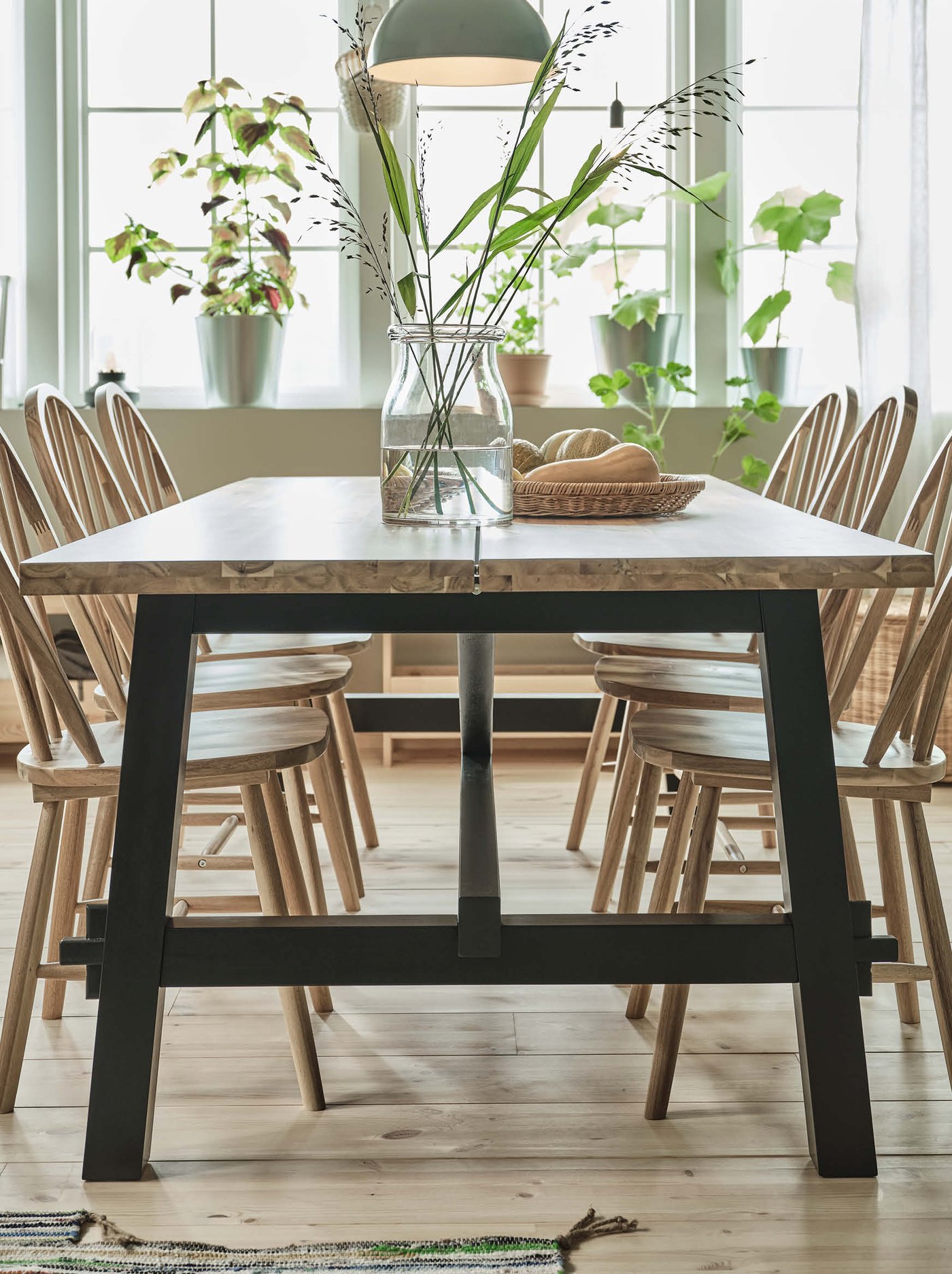 A wooden SKOGSTA dining table and six SKOGSTA chairs stand in a dining room under two SKURUP pendant lamps.