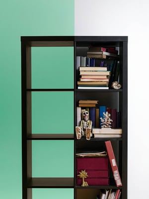 A partially filled IKEA KALLAX bookshelf creates a contrast between empty compartments and sections packed with books and small decorative items.