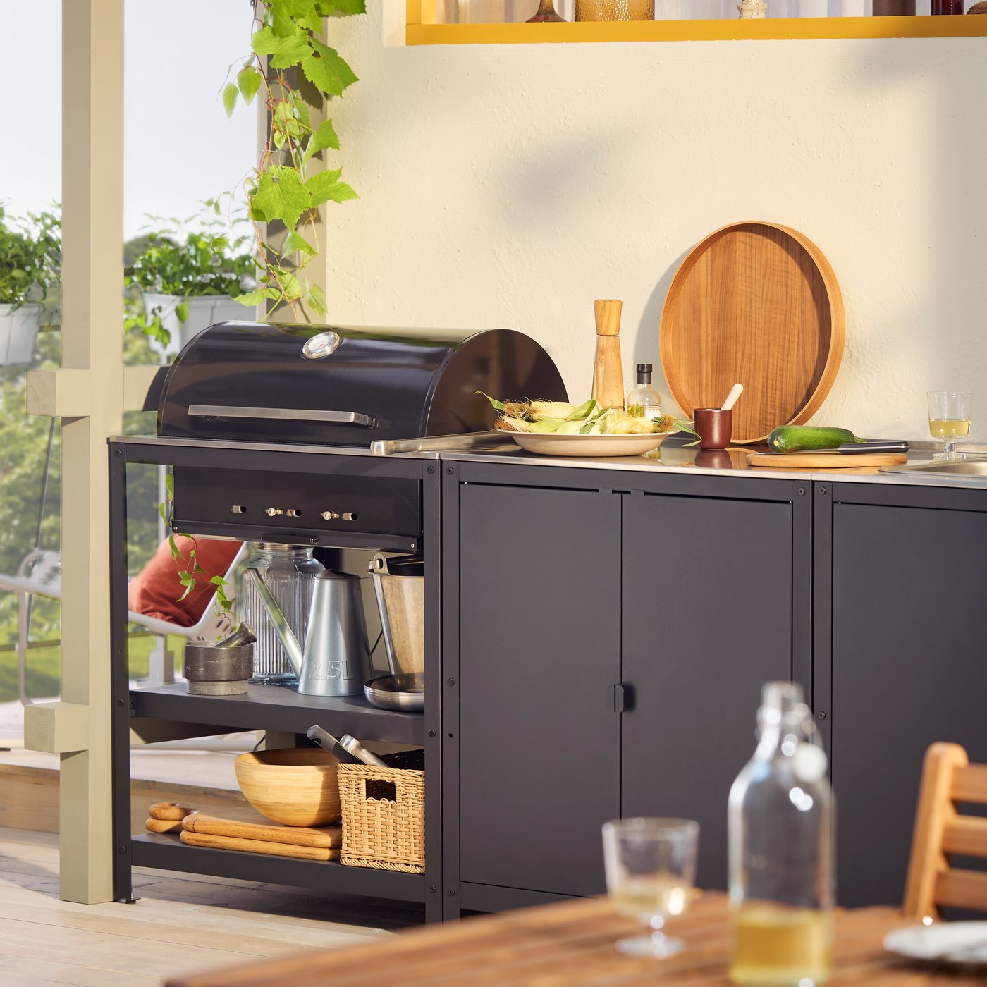 A veranda at sunset with a GRILLSKÄR outdoor barbeque and kitchen island in black stainless steel with cooking accessories.