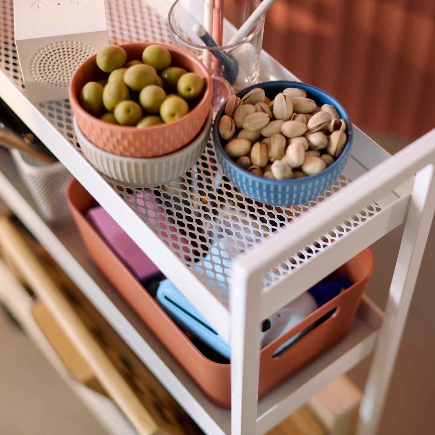 A close-up of a white NISSAFORS trolley that has items stored on the mesh shelves, including bowls of nuts and olives.