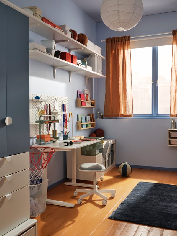 Un lado de una recámara infantil azul con estantes altos en la pared y un clóset blanco/azul SMÅSTAD/UPPFÖRA con 3 cajones.