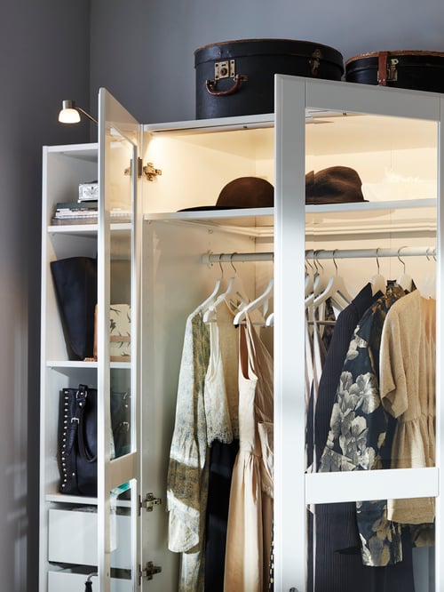 Dresses, hats and bags are stored in the top left portion of a PAX wardrobe with white/Tyssedal glass doors that are open.