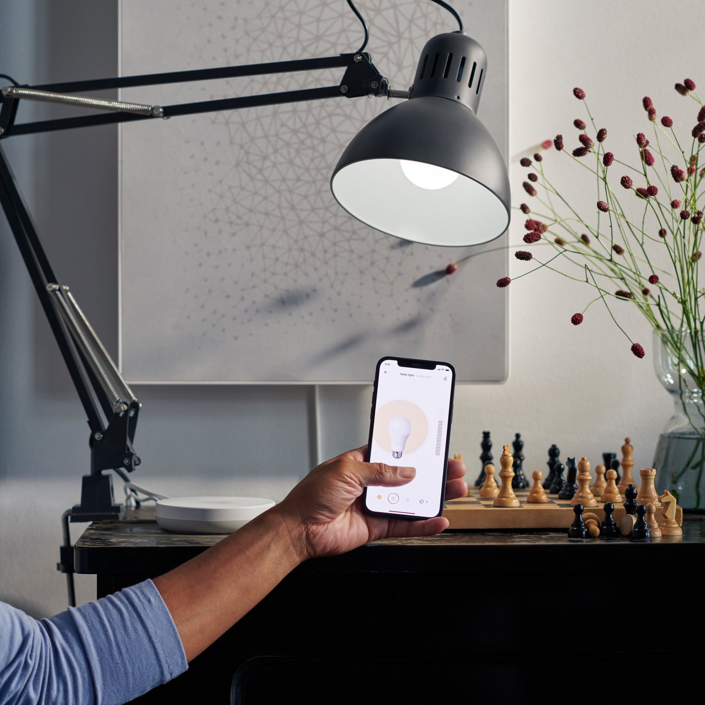 Person in picture with hand holding smartphone using IKEA Home Smart app to switch on TERTIAL work lamp