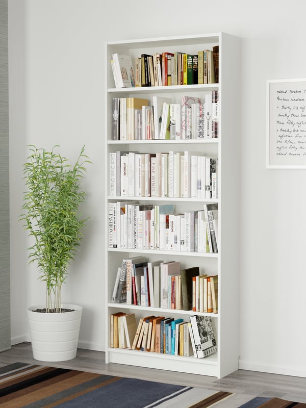 Ein weißes BILLY Bücherregal  80 breit, 28 tief und 202 cm hoch, steht vor einer weißen Wand. Daneben steht eine Zimmerpflanze. 