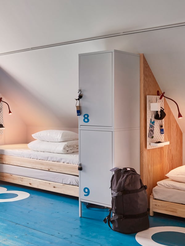 A bedroom with sloped ceiling and blue floor showing two sleeping areas with wooden UTÅKER beds and lockable cabinets.
