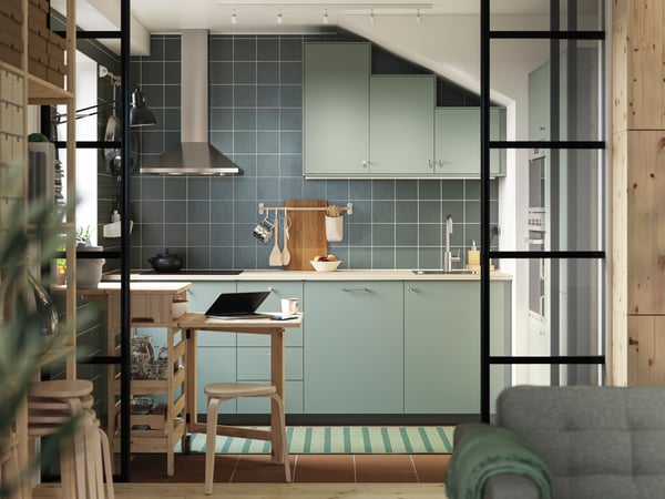 Une cuisine verte en L est équipée de façades NICKEBO gris vert et d'une table mobile RESARÖ à abattant avec rangement et quelques tabourets.