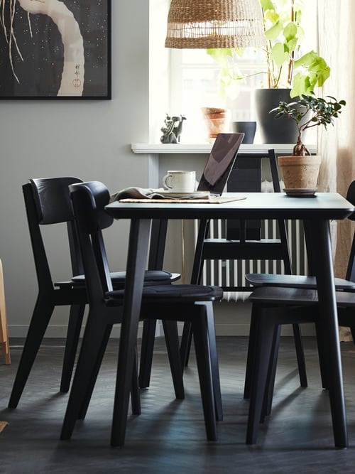 Dining room with a rectangular table, multiple black chairs, a mug, and a potted plant. A pendant lamp shade is in the back.