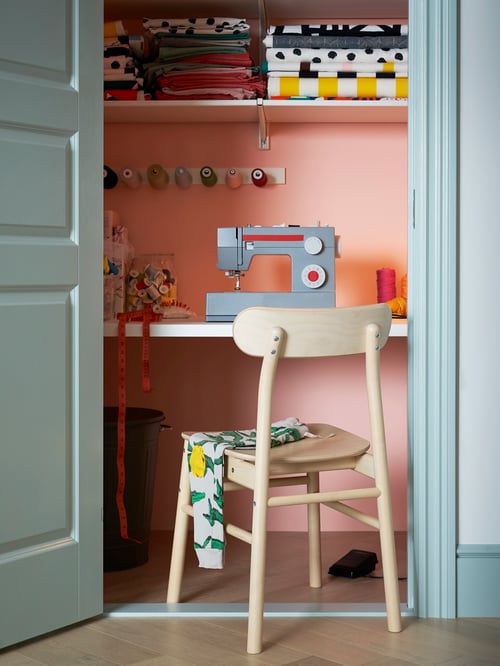 Room with RÖNNINGE chair, ALGOT wall shelve, sewing machine, sewing yarn, multiple throws and other items.